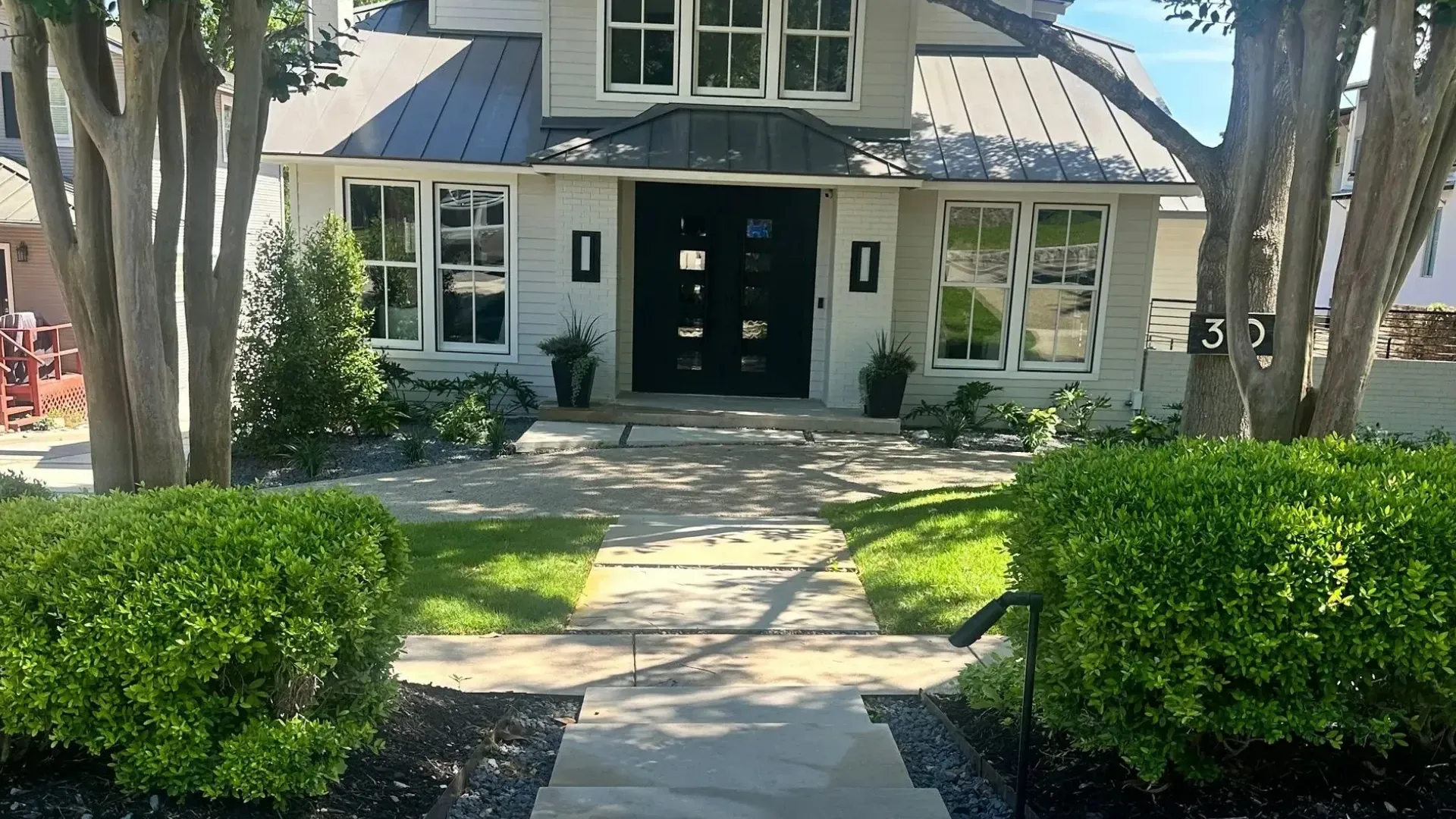 Gray house with a dark door, approached by a stone path lined with hedges and trees.