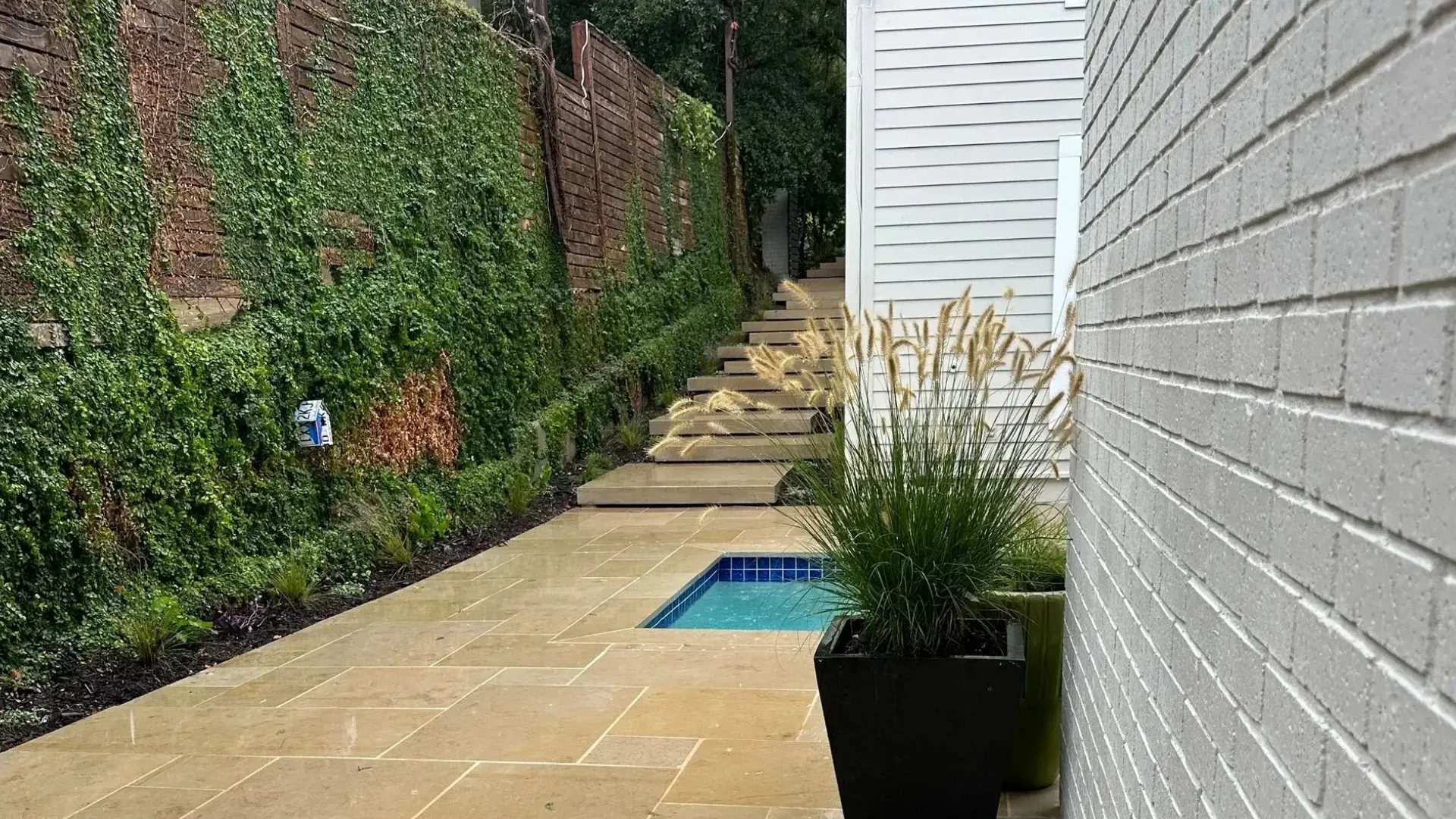 Stone path alongside a white brick wall and a climbing-vine covered wall, leading to a small pool.