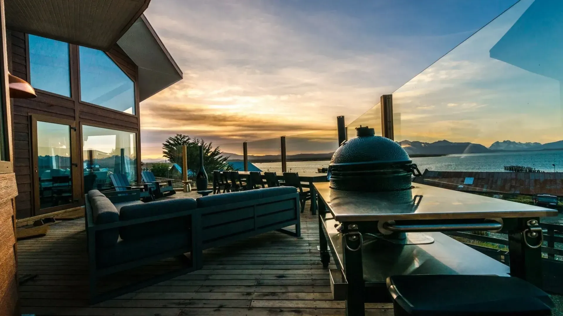 Outdoor deck with grill, seating, and ocean view at sunset.