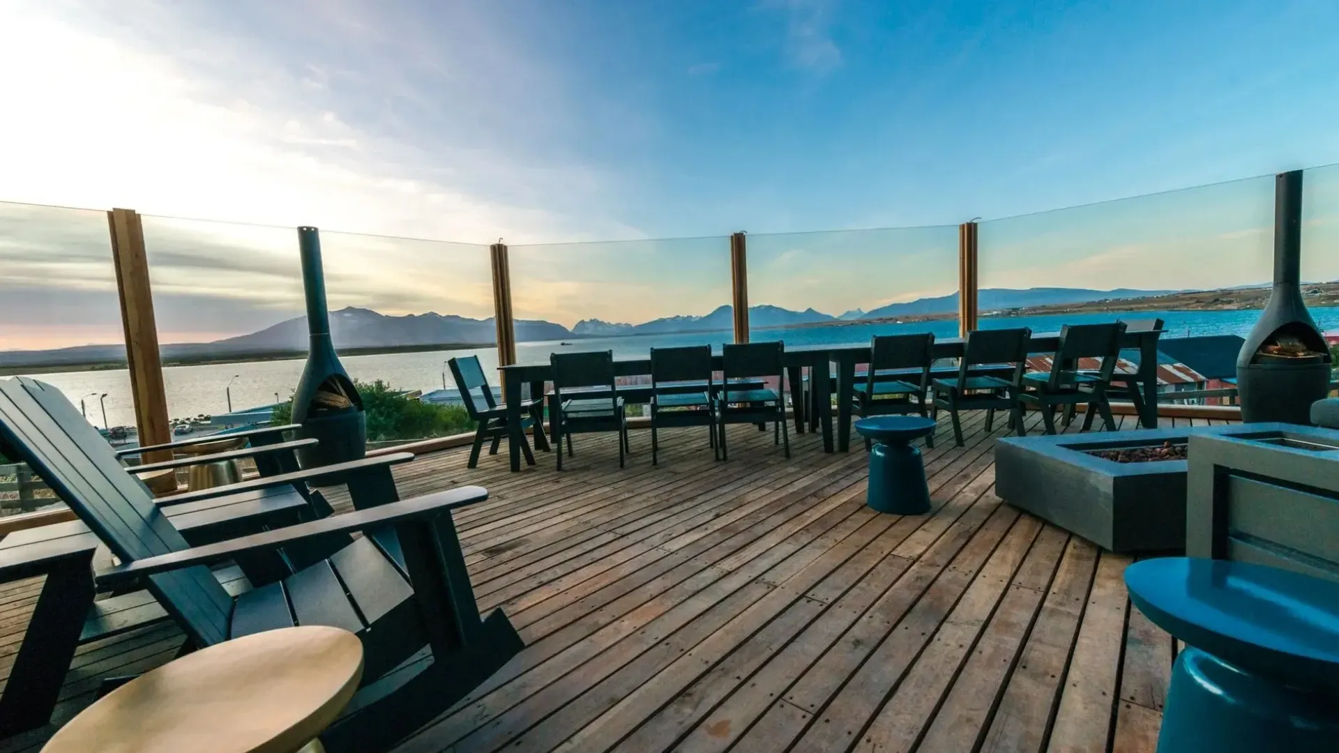 Wooden deck overlooking water with outdoor furniture and fire pits.