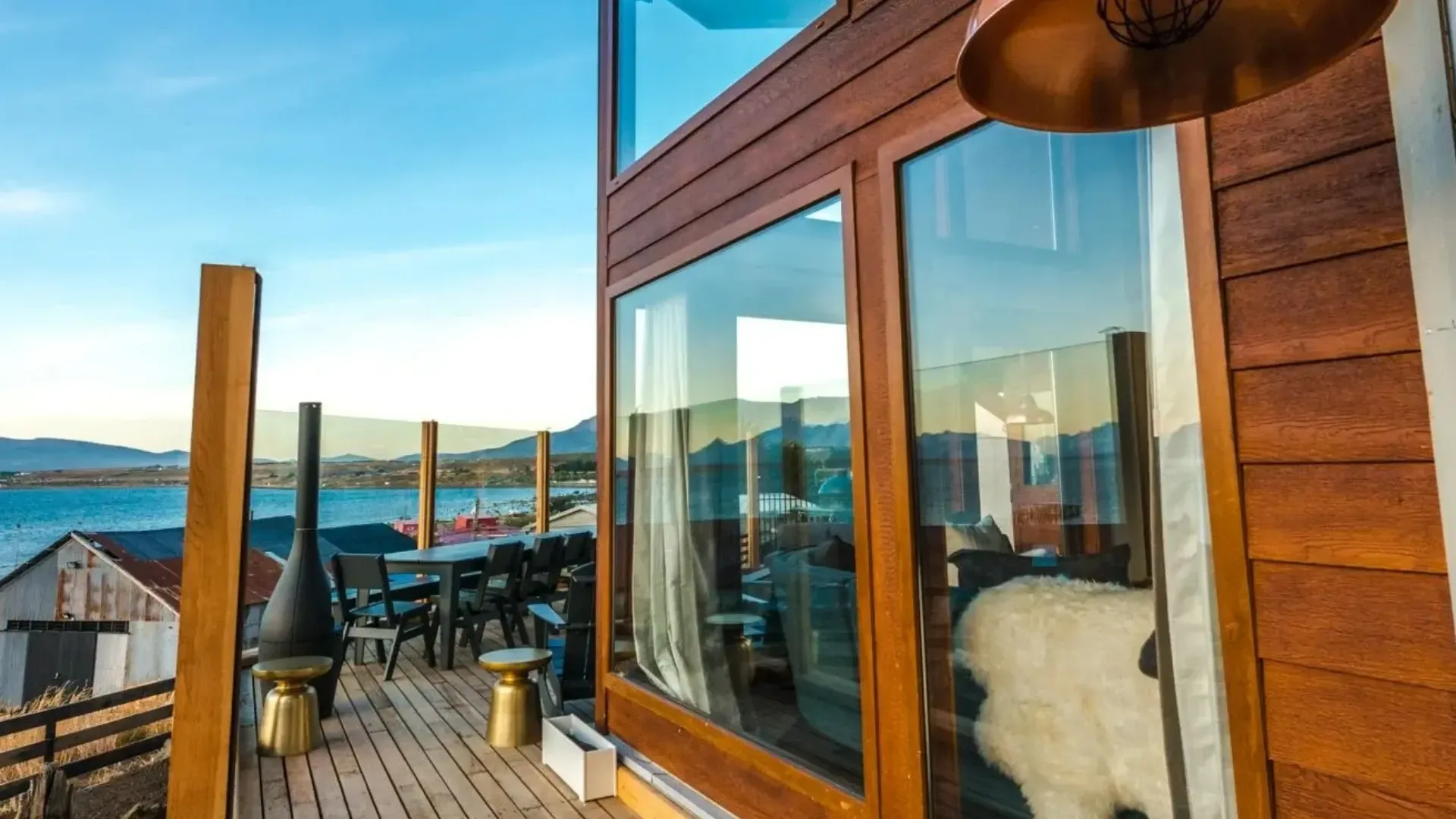Wooden cabin with deck overlooking water, large window, copper light fixture.