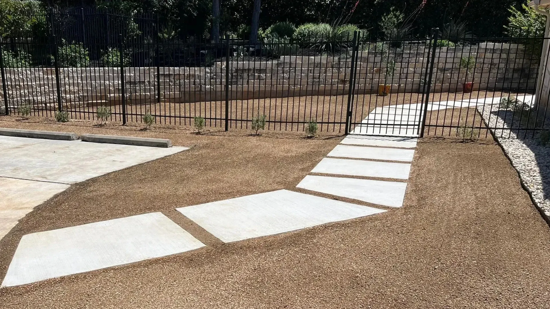 Stone pathway through gravel landscaping, leading to a wrought iron gate.