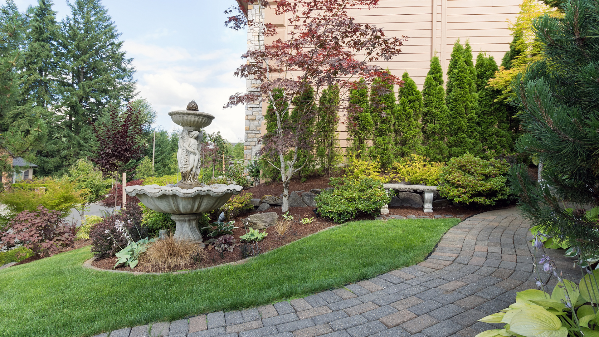 Stone patio leads to a pool, framed by rocks, lavender, and trees, in a sunny outdoor setting.