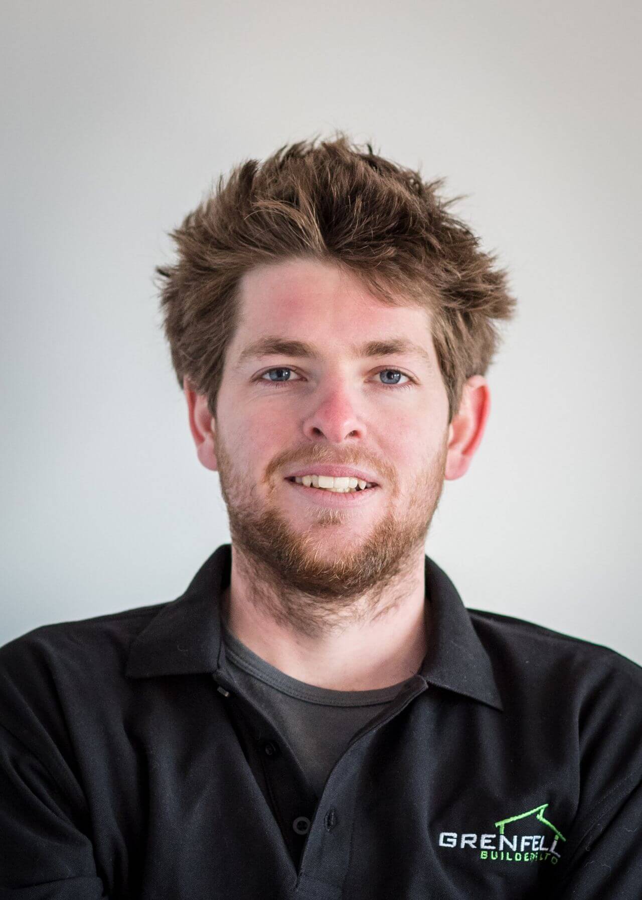 a man with a beard is wearing a black polo shirt and smiling .