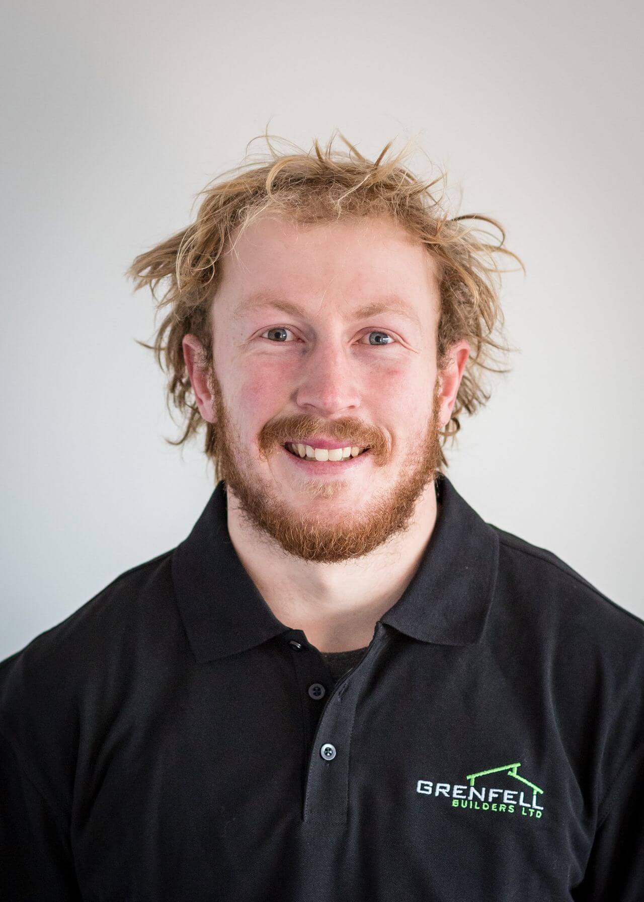 a man with a beard is wearing a black polo shirt and smiling .