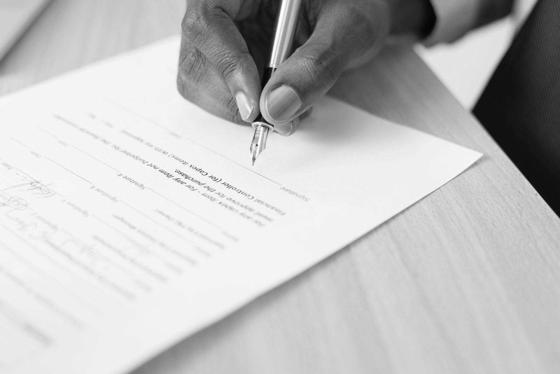 Close-up of a hand signing official documents on a wooden desk, representing the efficient processing of forms for fast police clearance.