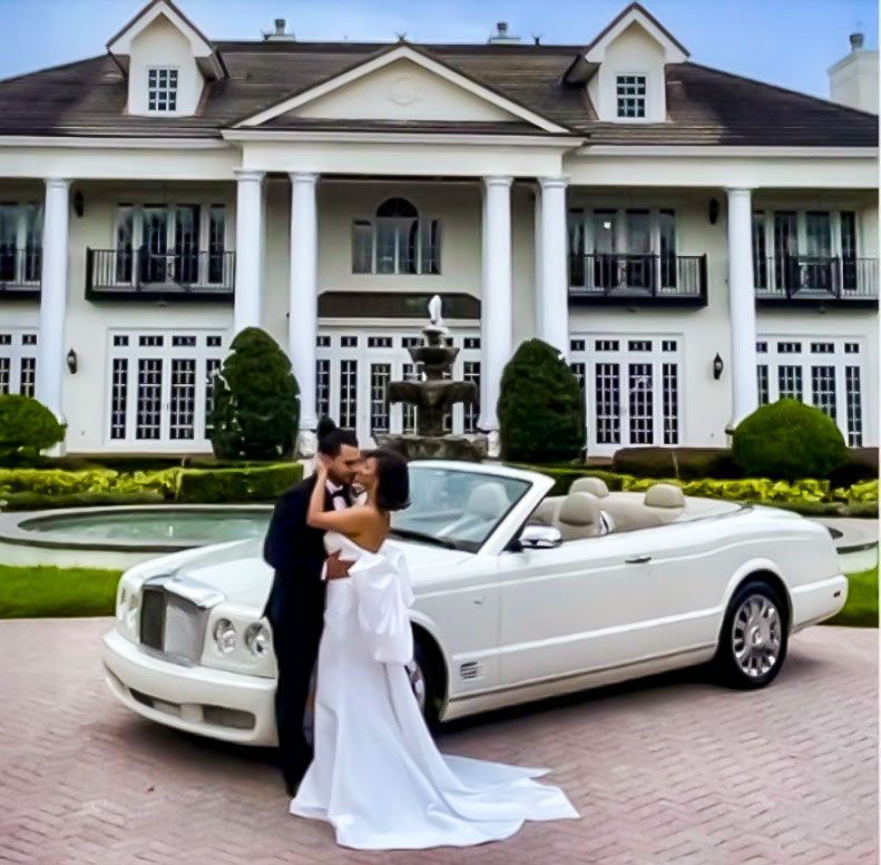 Exotic Limo Orlando Couple embraces in front of a white convertible car and large mansion with fountain.