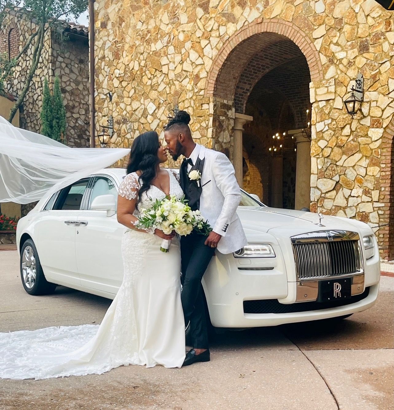 Newlyweds share a tender moment next to a white Rolls Royce. She wears a white gown, and he wears a white suit.Exotic Limo Orlando