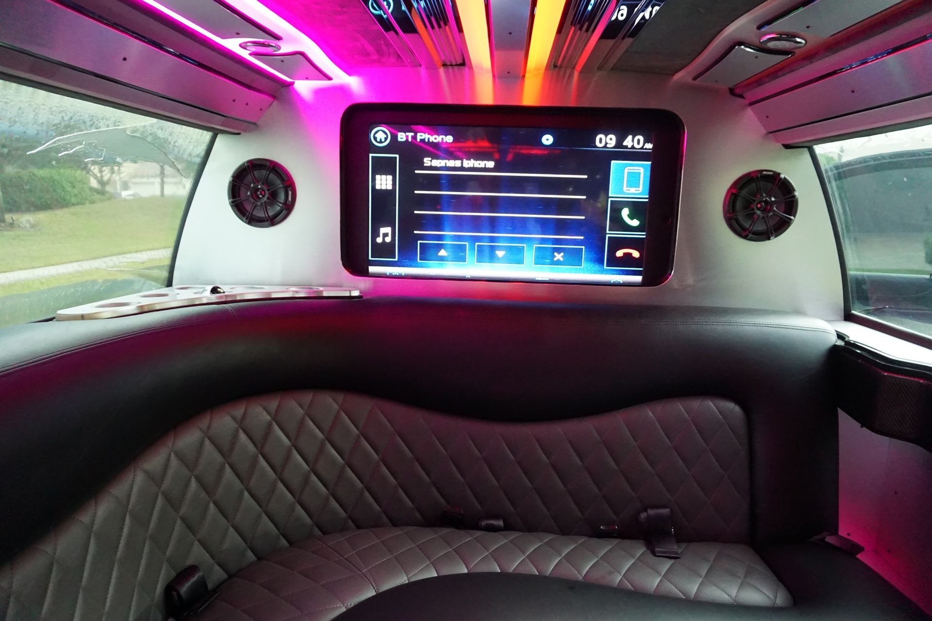 Interior of a limousine with black and gray quilted seating, a large screen, and pink and gold lights.Exotic Limo Orlando
