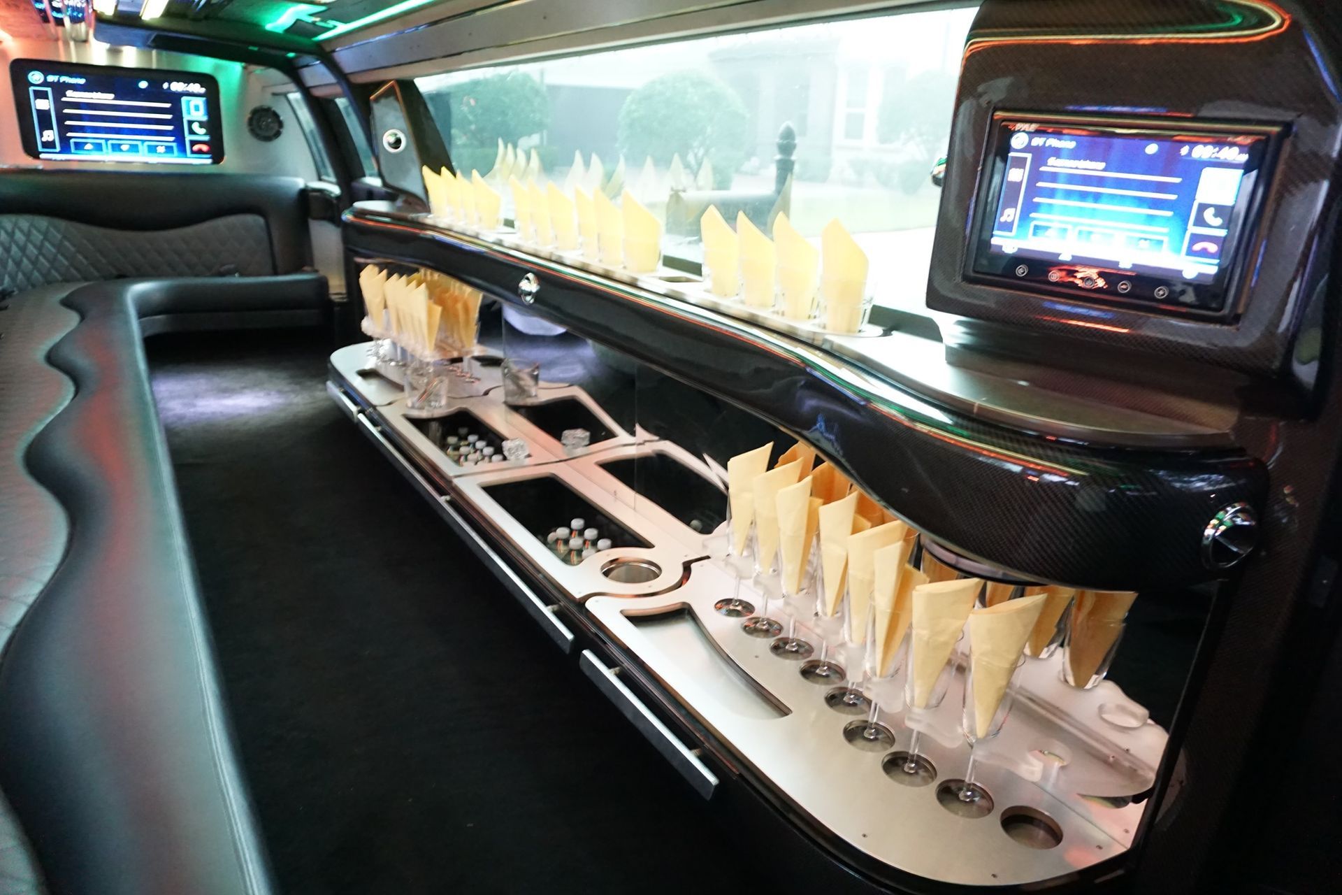 Interior of a limousine, featuring a bar with compartments, cup holders, and two screens displaying media.Exotic Limo Orlando