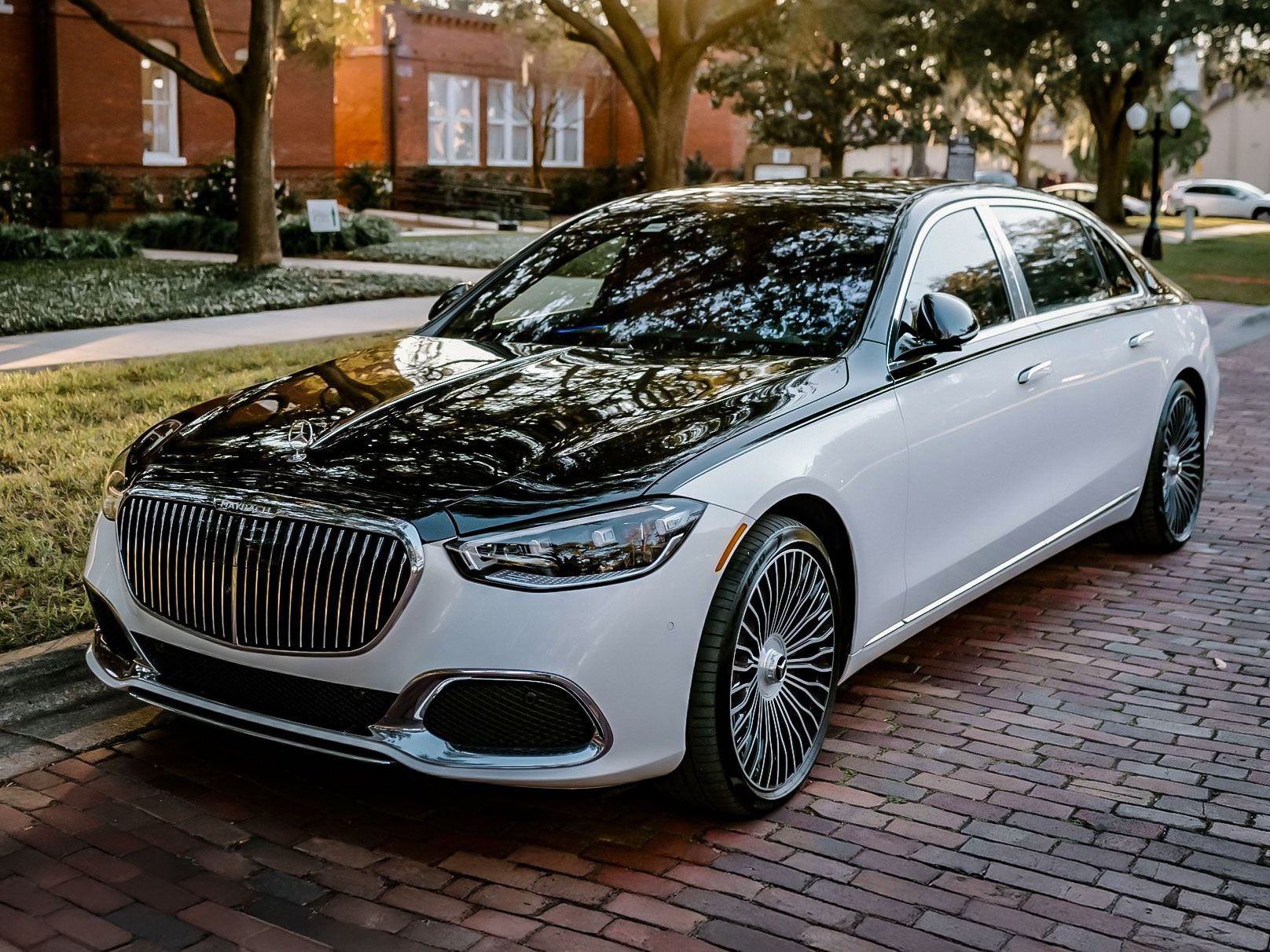 White and black luxury car parked on a brick path, with a shiny grill and intricate wheels.