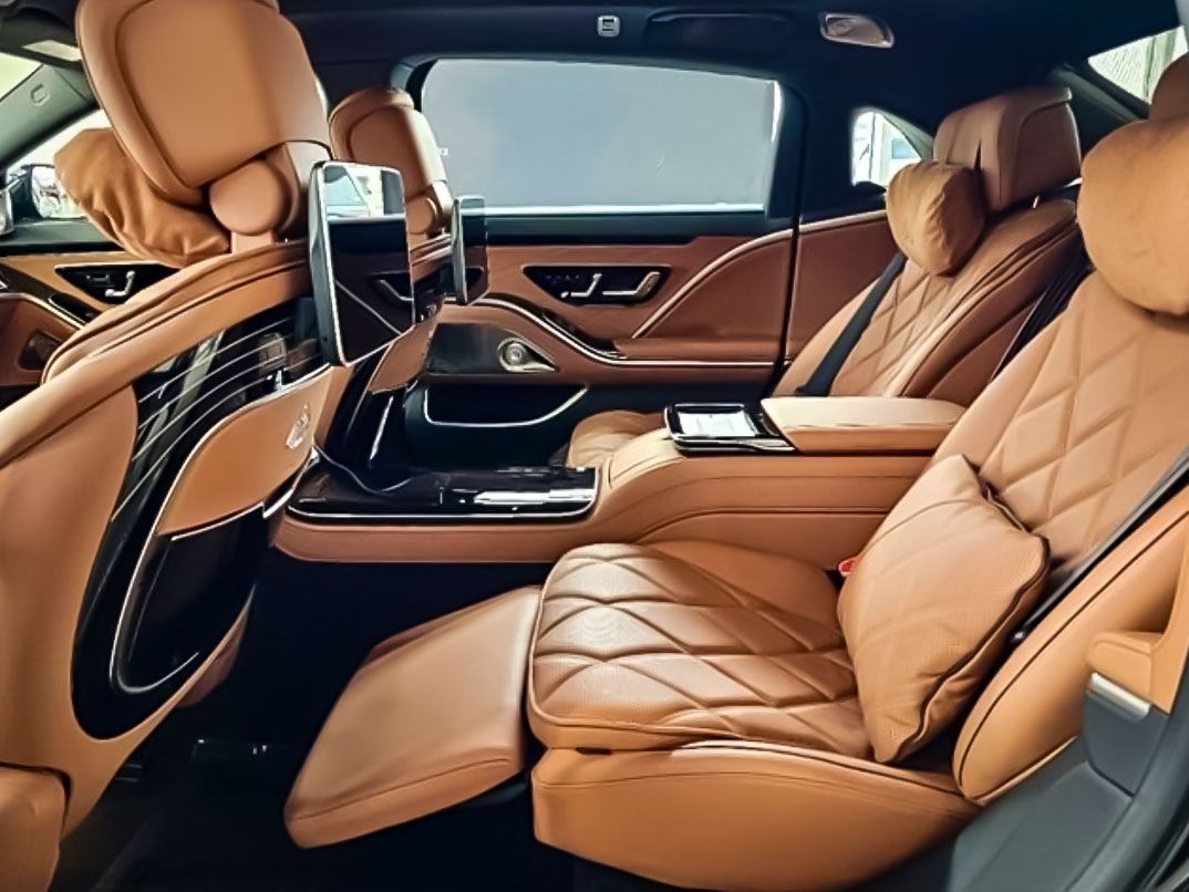 Tan leather interior of a luxury car with reclined rear seats, a center console, and headrests.