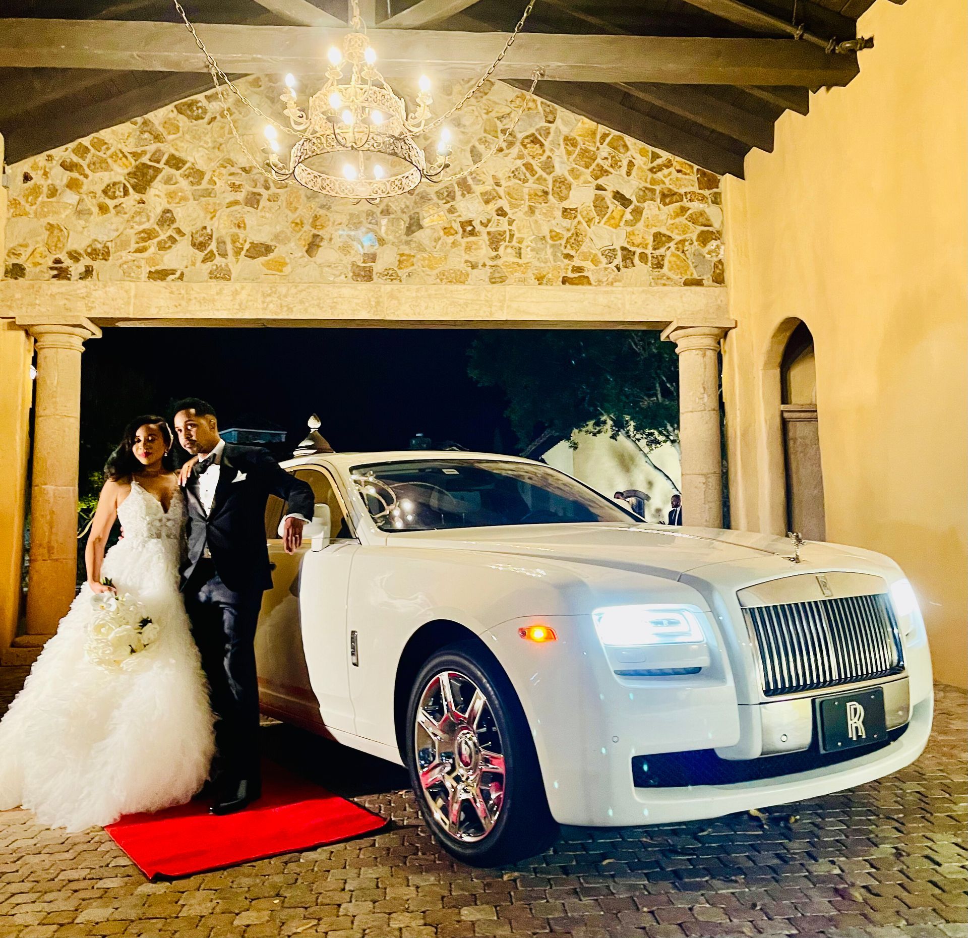 Exotic Limo Orlando Bride and groom pose with a white Rolls-Royce outside a stone building.