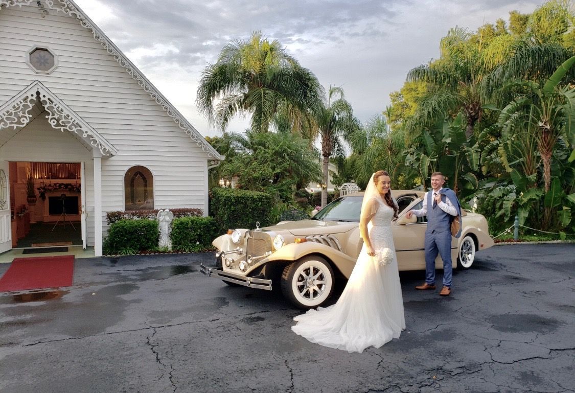 Exotic Limo Orlando Bride and groom pose by a vintage car outside a white chapel after their wedding.