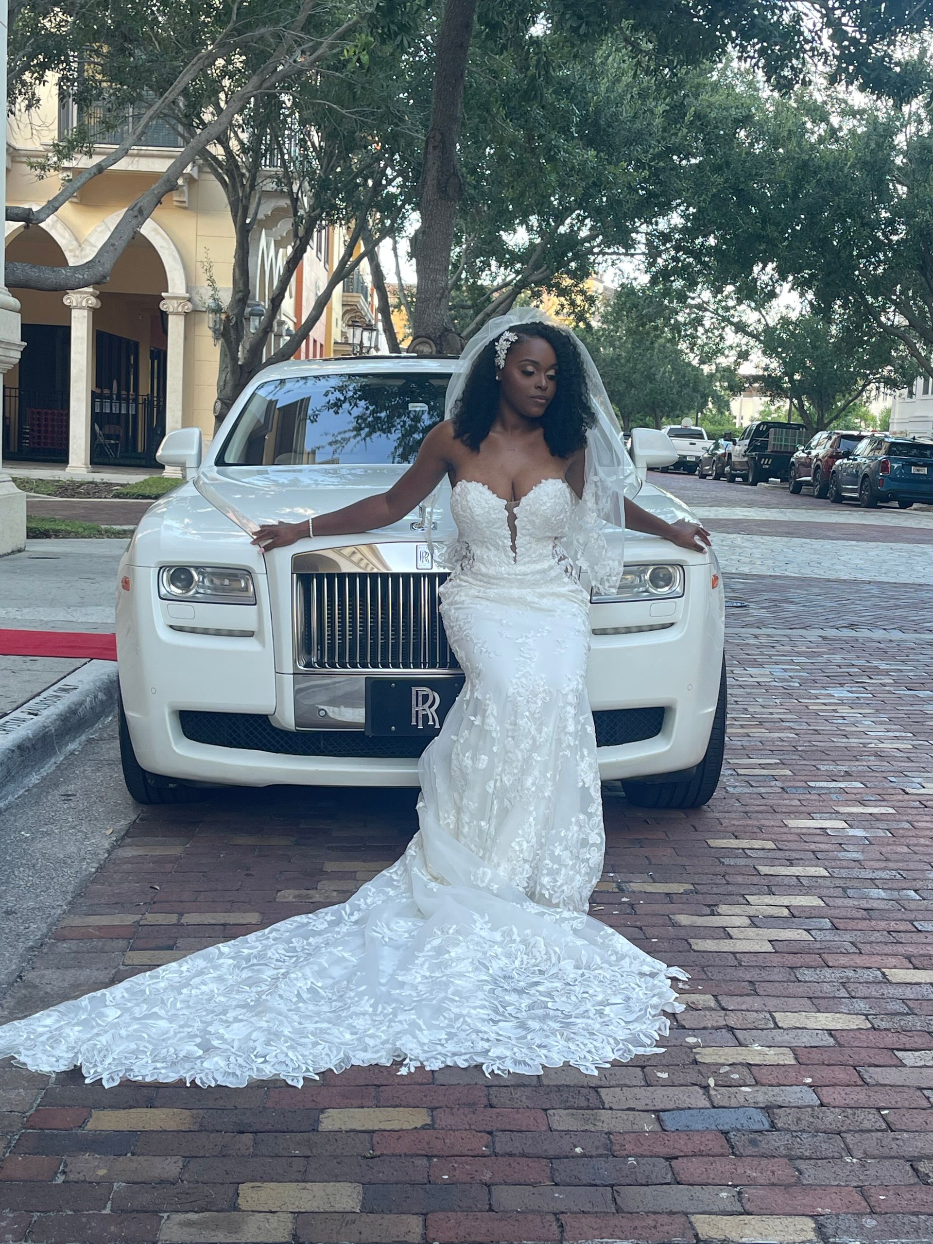Exotic Limo Orlando Bride in a white, ornate wedding gown with a long train poses in front of a white Rolls Royce.