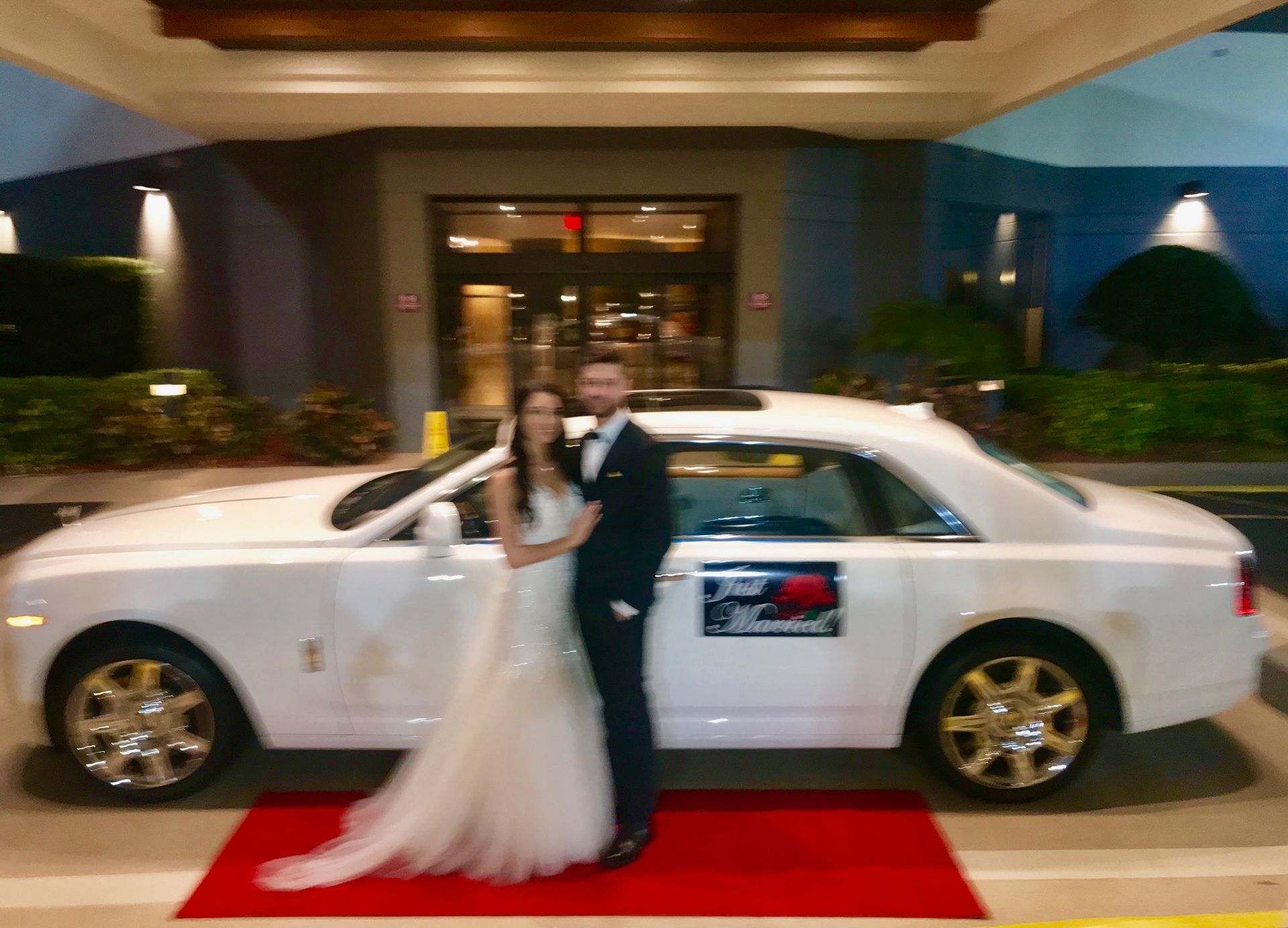 Exotic Limo OrlandoNewlyweds pose next to a white Rolls Royce on a red carpet in front of a building entrance.