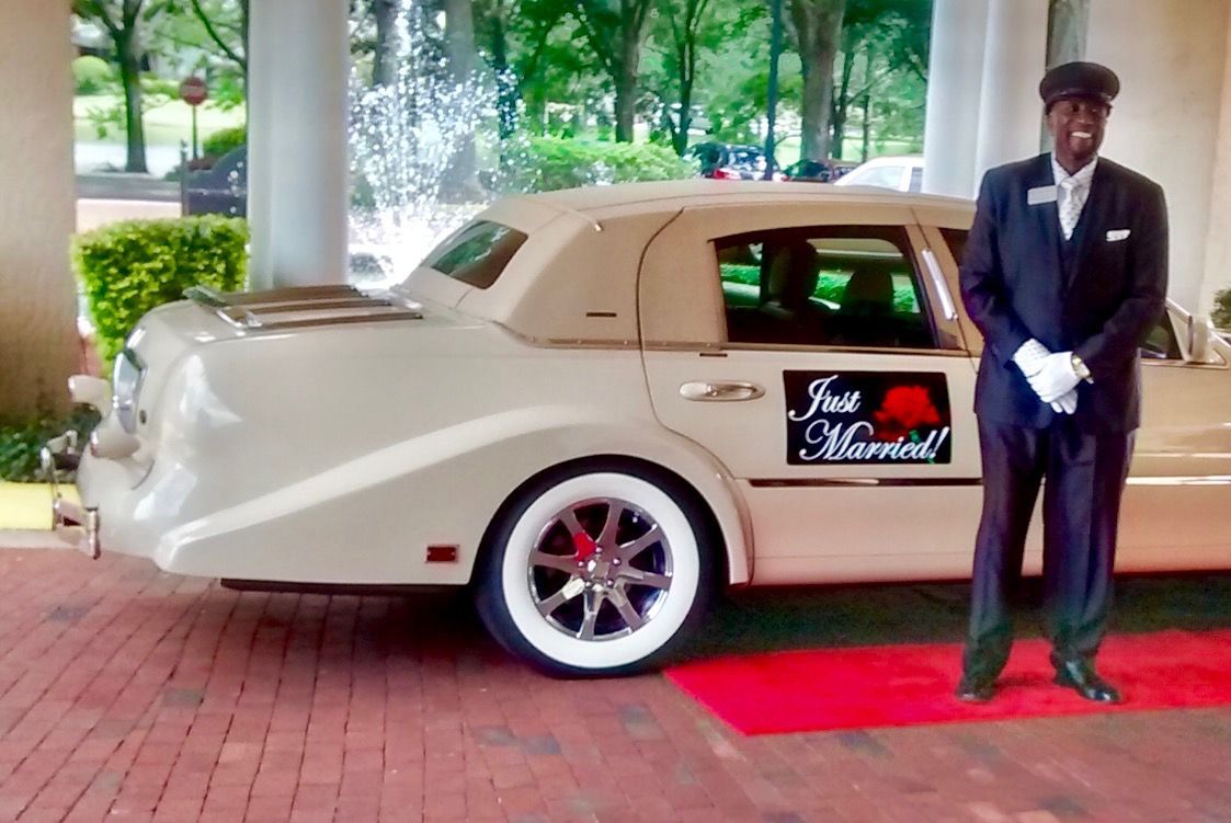 Man in uniform stands beside a cream-colored limousine with 