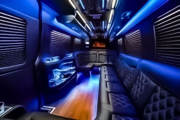 Interior of a luxury party bus with blue LED lighting, quilted leather seating, and a wooden floor.