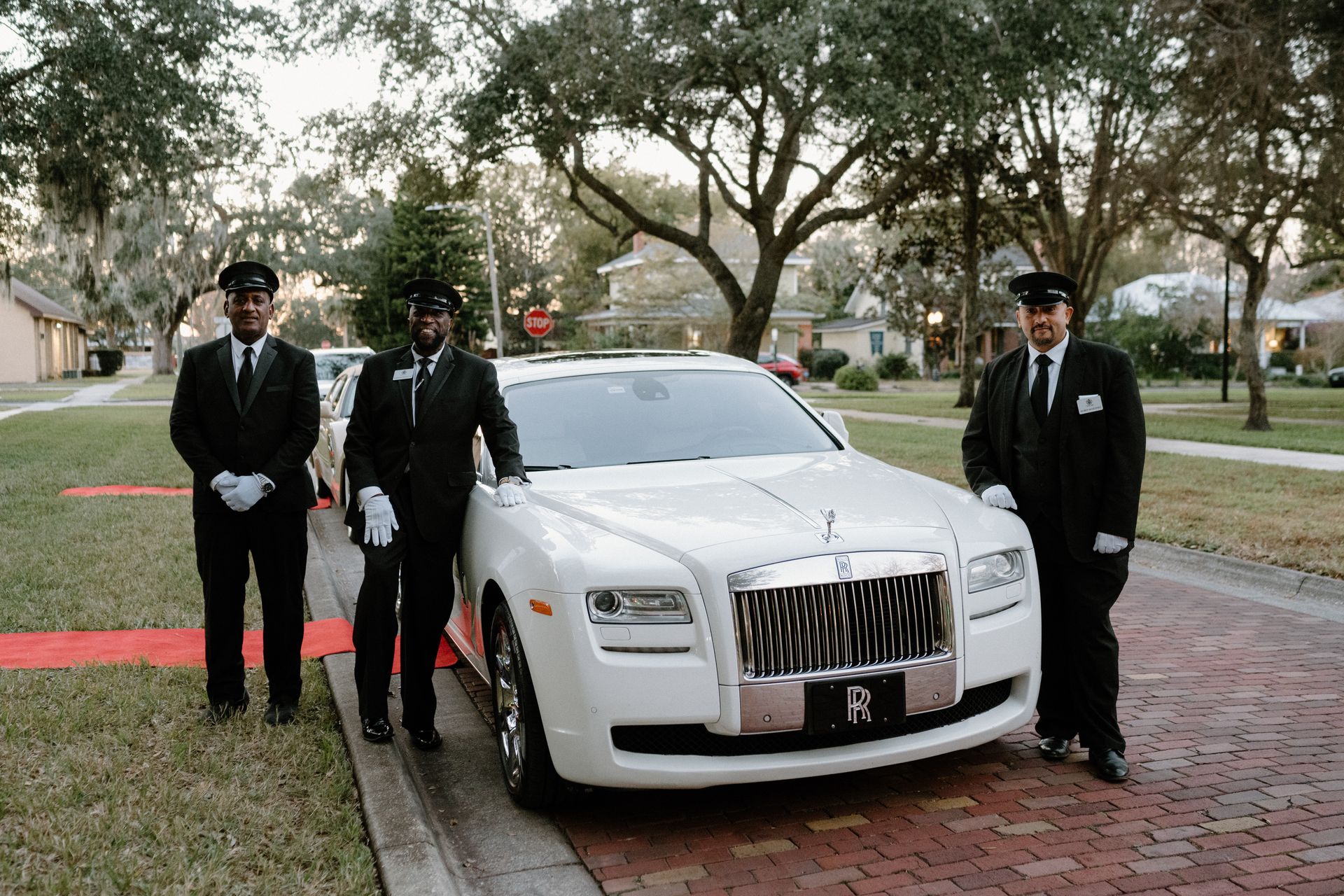 Exotic Limo Orlando Three people in black suits and white gloves stand with a white Rolls Royce on a brick street.
