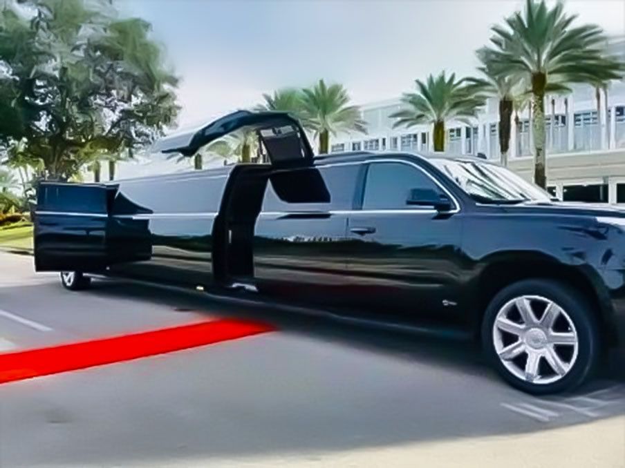 Black limousine with open doors on a red carpet, parked on a street with palm trees and a building in the background.Exotic Limo Orlando