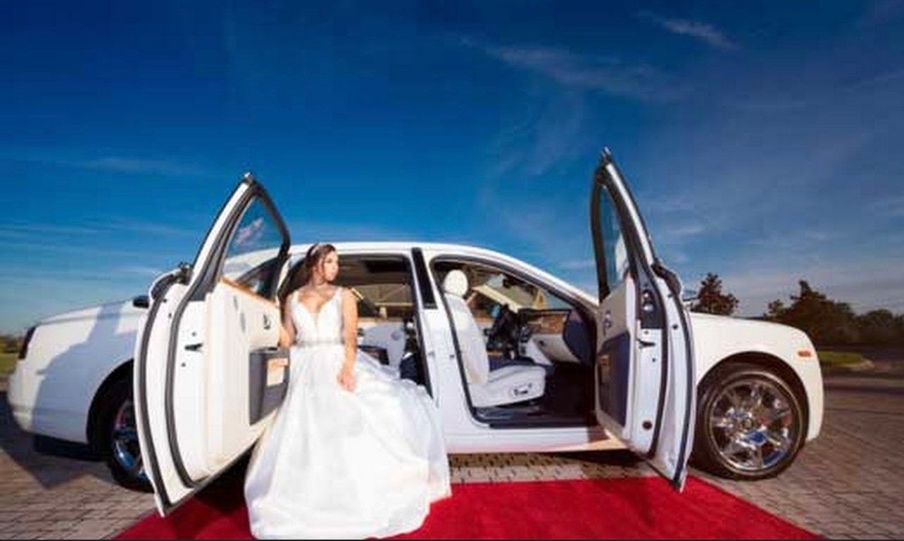 Exotic Limo Orlando Bride in white wedding dress exits a white luxury car with open doors on a red carpet, blue sky in the background.