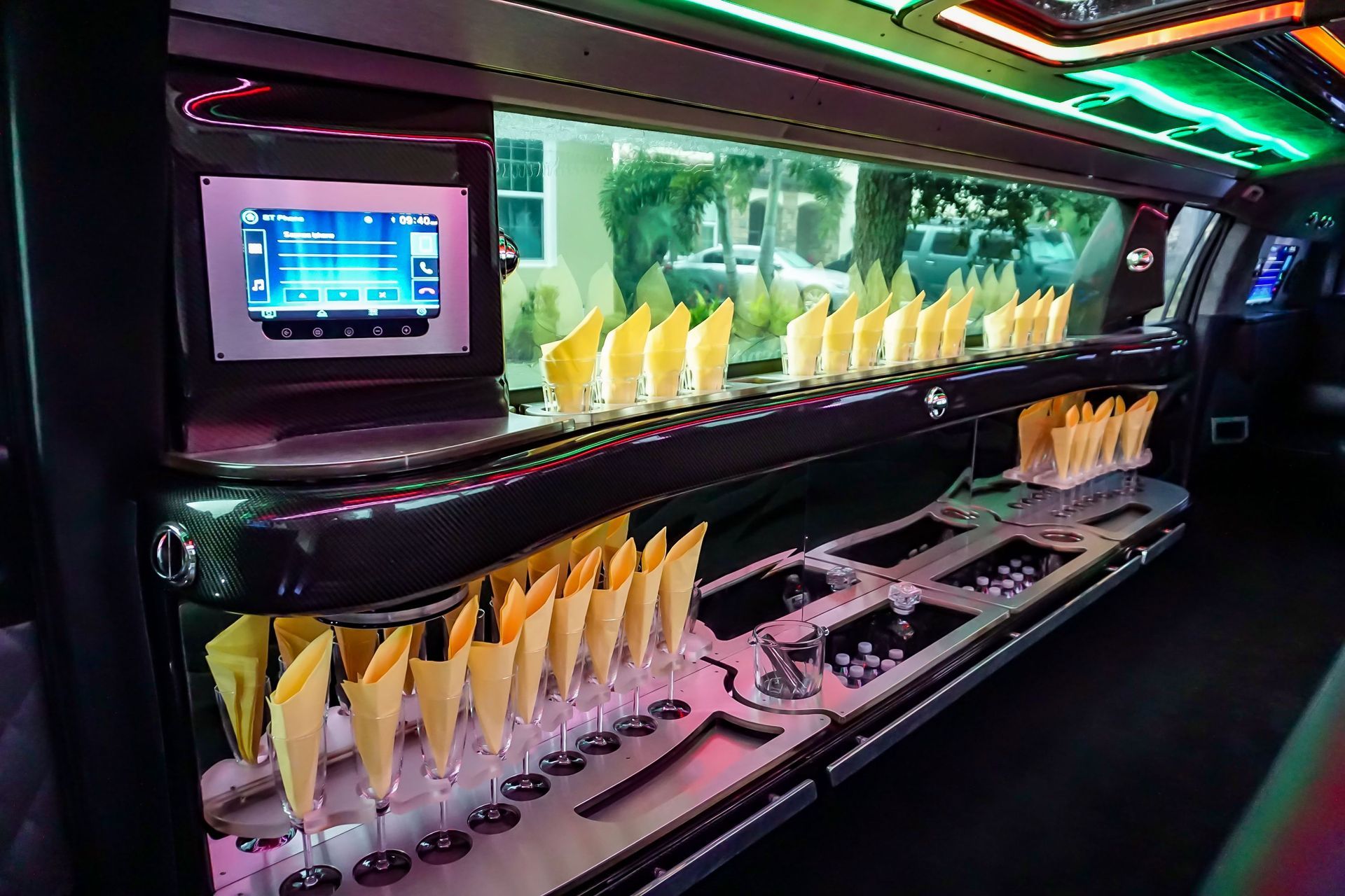 Interior of a limousine with champagne flutes, drinks, and a screen; neon lights illuminate the space. Exotic Limo Orlando