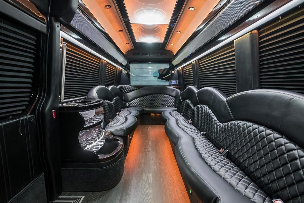 Interior of a luxury black party bus with leather seating, ambient lighting, and a large screen.