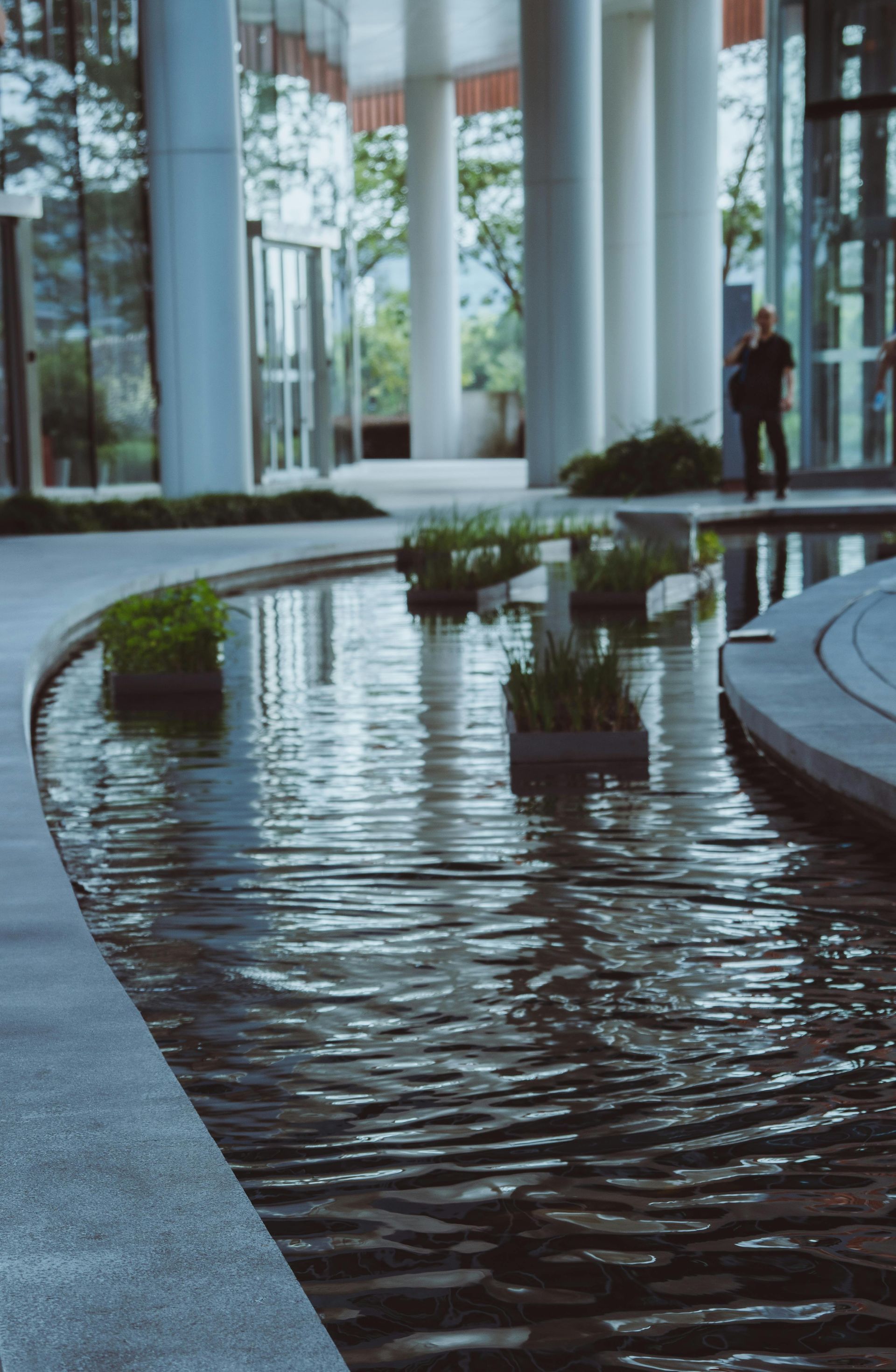 Modern lobby with a reflecting pool, tall white columns, and a person standing near the windows