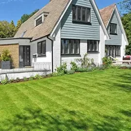 People landscaping a green house with a porch, stone accents, and a lush front lawn.
