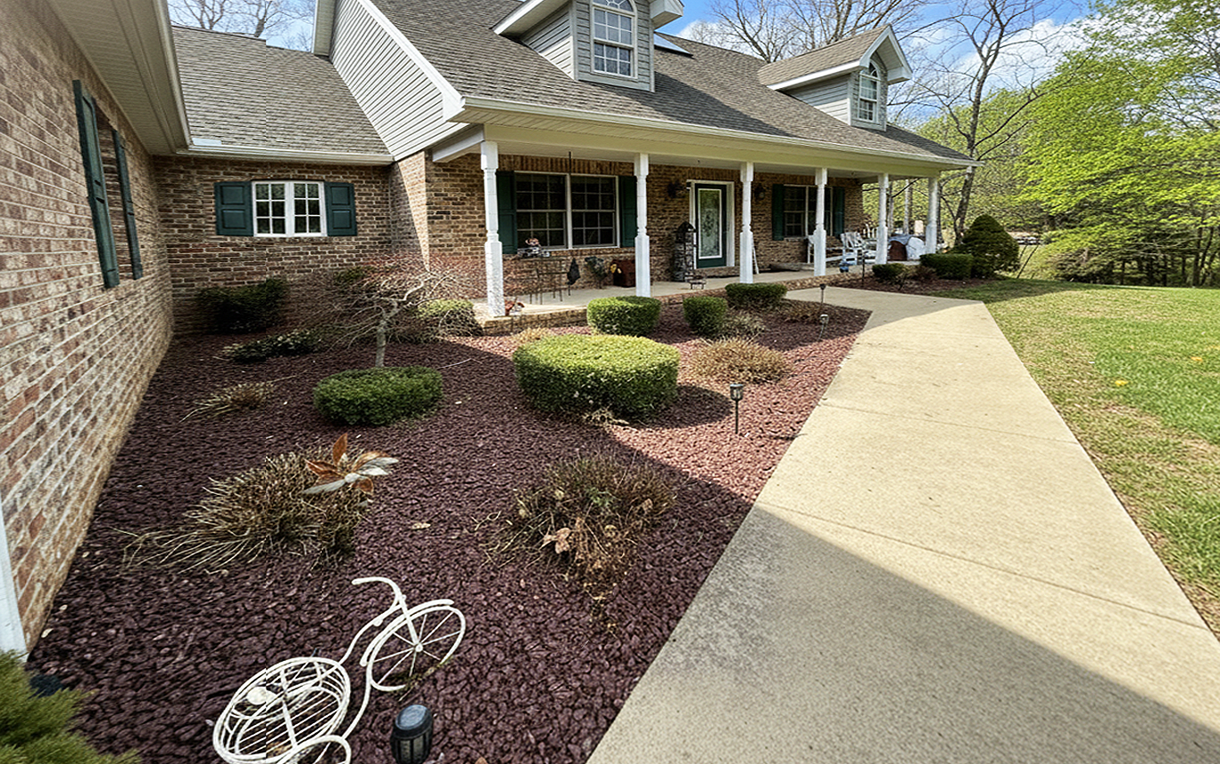 Brick house with covered porch, landscaped front yard, and concrete walkway alongside a mulch bed