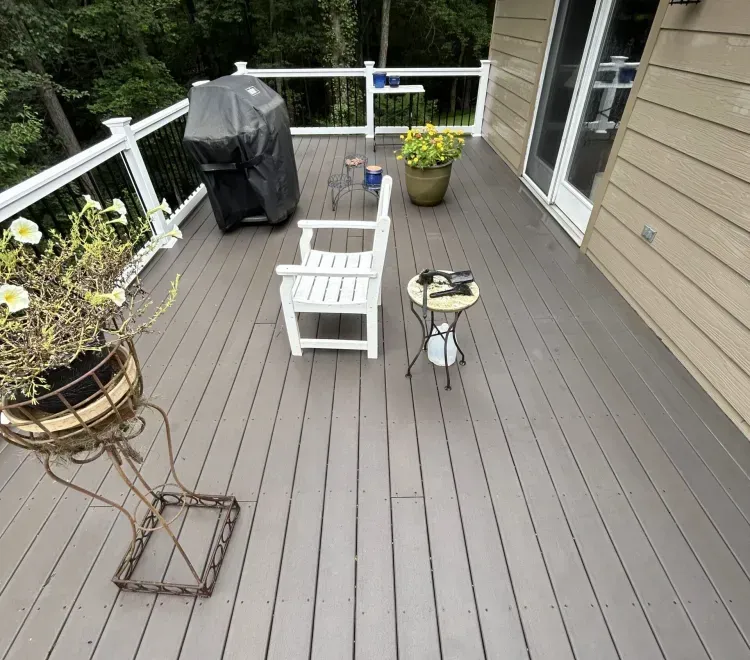 Rainy wooden deck with white railing, potted plants, and a covered grill overlooking trees