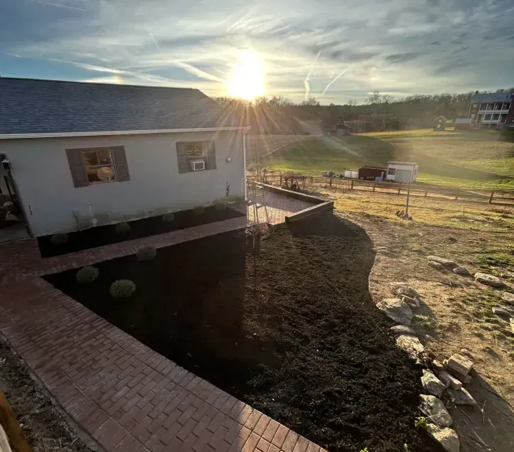 Brick walkway leading to a white house with two windows, front lawn, and bright sunlight