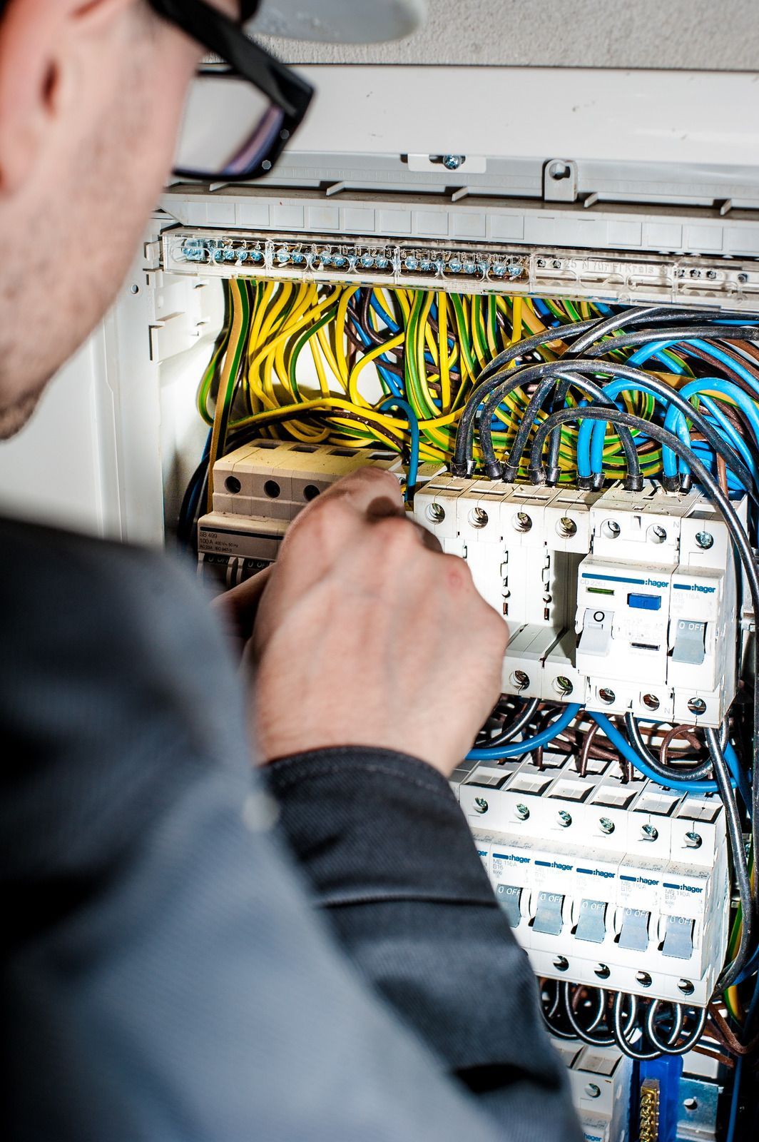 Electrician working inside an open electrical panel with wires and circuit breakers.