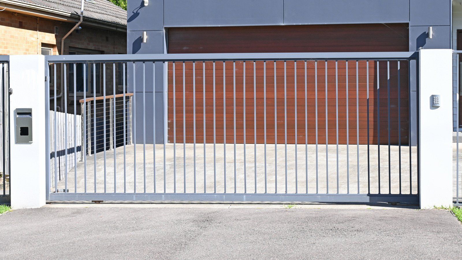 Gray metal gate in front of a modern house with a brown garage door.
