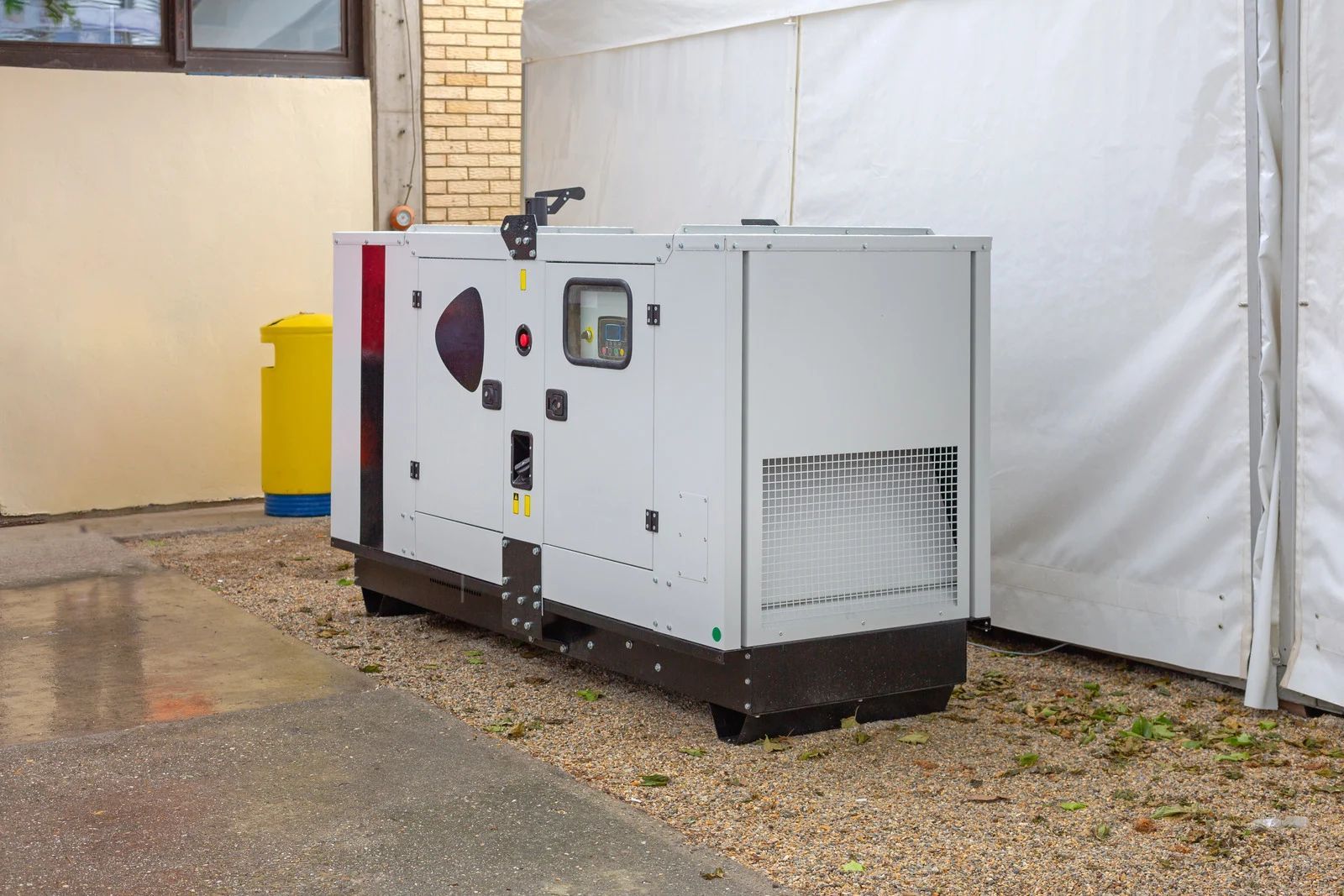 White industrial generator unit outdoors beside a building and tented area.