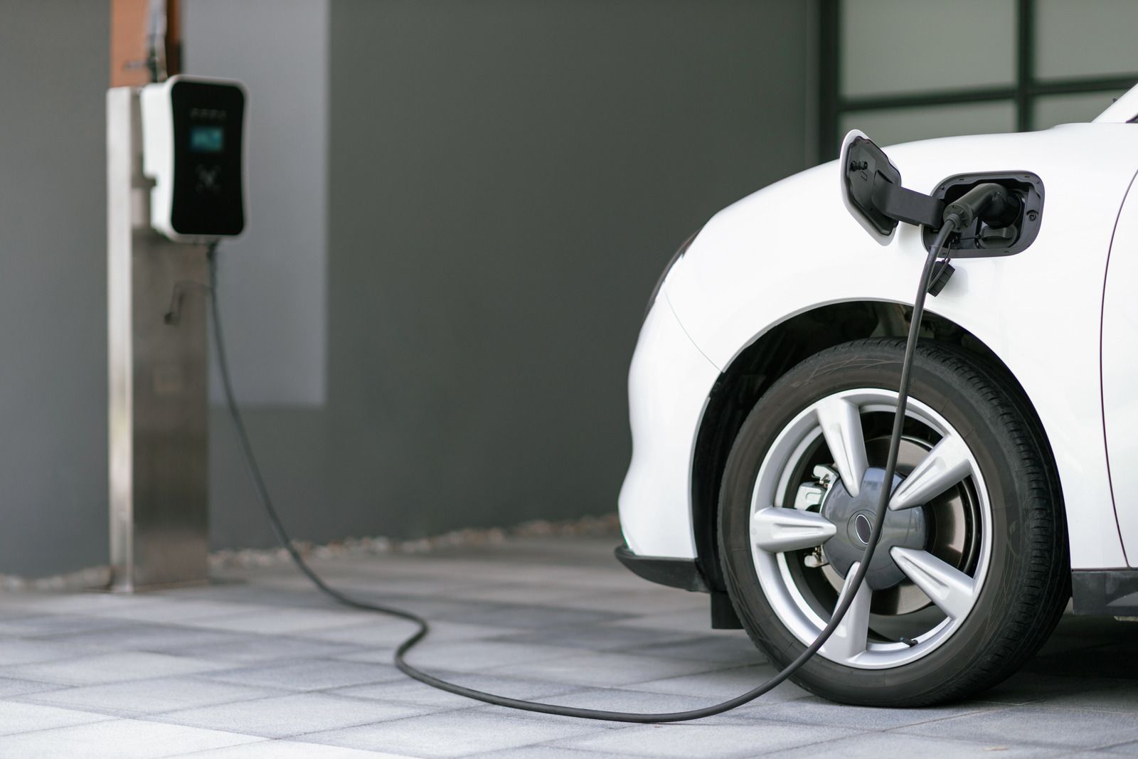 White electric car charging outdoors at a home charging station.