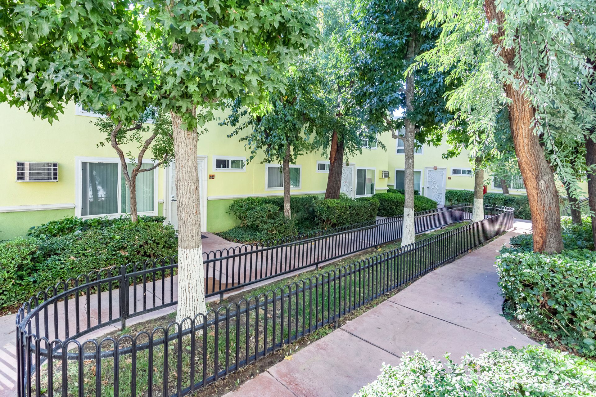 A walkway leading to a building with a fence and trees in front of it.