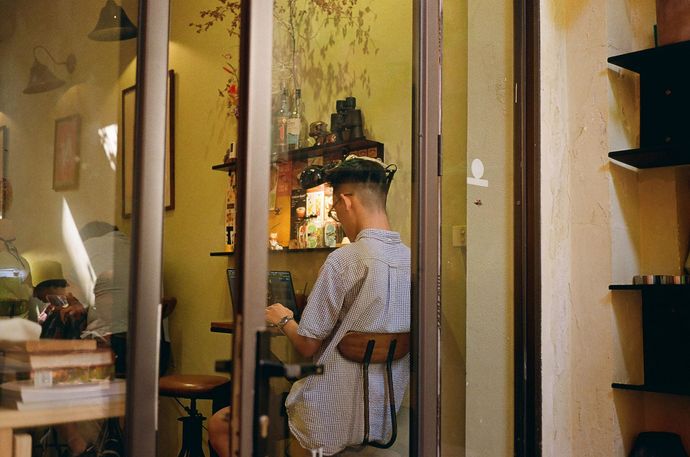 A man is sitting at a table in a room behind a glass door.