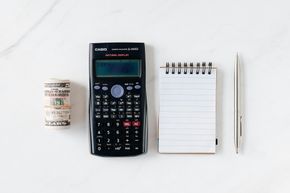 A calculator , a notebook , and a pen are on a table.