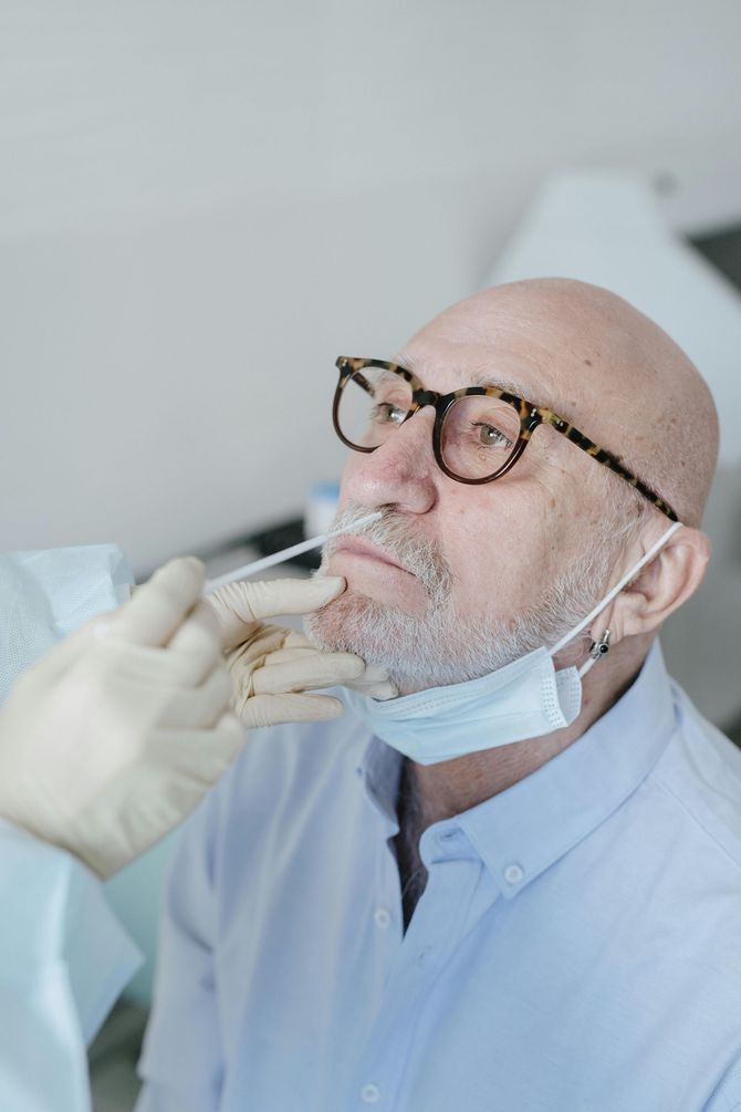 A man with glasses and a beard is getting a swab from his nose.