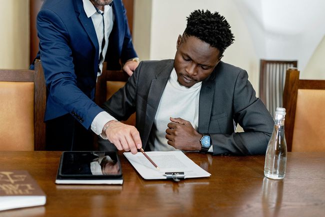 A man in a suit is sitting at a table with a tablet and a clipboard.