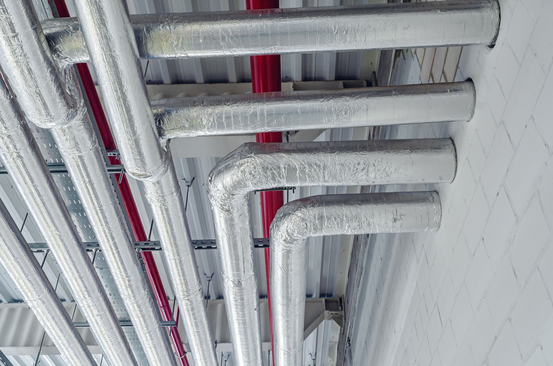 Steam piping system insulation on ceiling-mounted metal pipes at a modern industrial facility. Steam piping system insulation on ceiling-mounted metal pipes at a modern industrial facility.