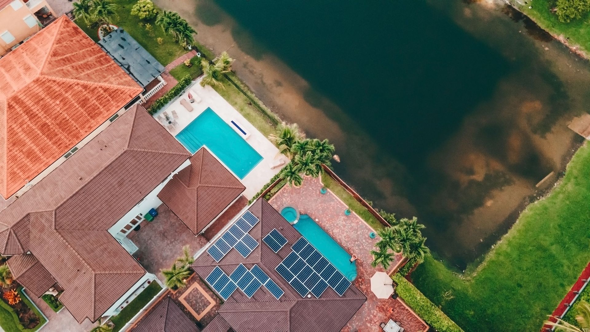 Aerial view of a house with a blue pool beside a river and green lawn
