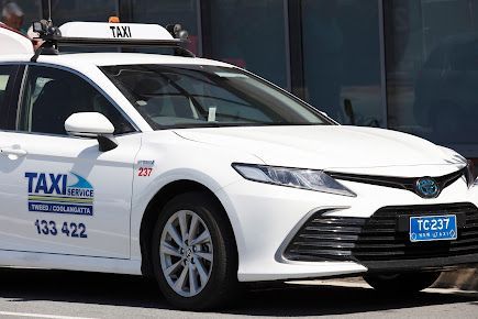A White Taxi is Parked in Front of a Building — Tweed Heads Coolangatta Taxi Service In Tweed Heads, NSW