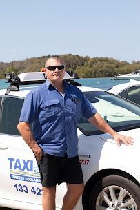A Man in a Blue Shirt is Standing Next to a White Taxi — Tweed Heads Coolangatta Taxi Service In Coolangatta, QLD