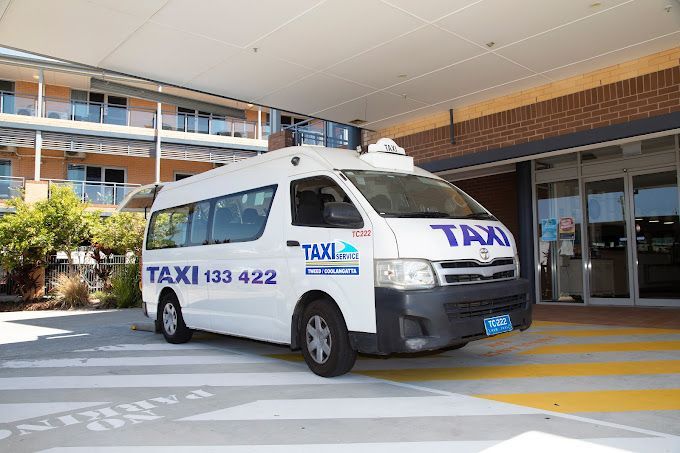 A White Taxi Van is Parked in Front of a Building — Tweed Heads Coolangatta Taxi Service In Tweed Heads, NSW