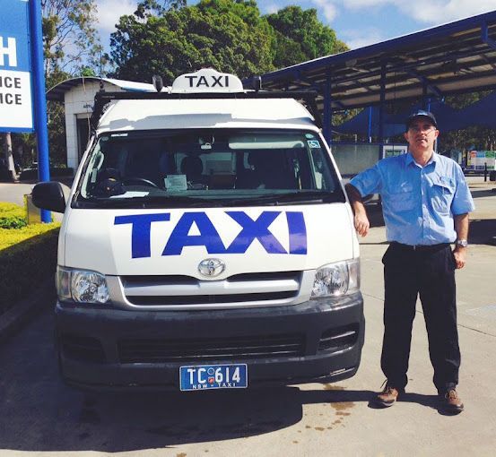 A Man Stands in Front of a White Taxi — Tweed Heads Coolangatta Taxi Service In Tweed Heads, NSW