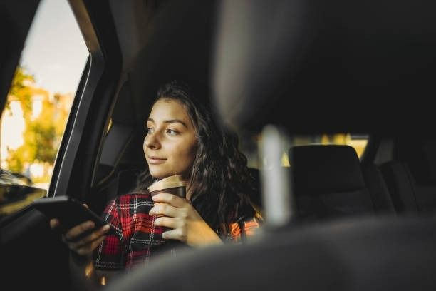 A Woman is Sitting in the Car Looking at Her Phone — Tweed Heads Coolangatta Taxi Service In Tweed Heads, NSW