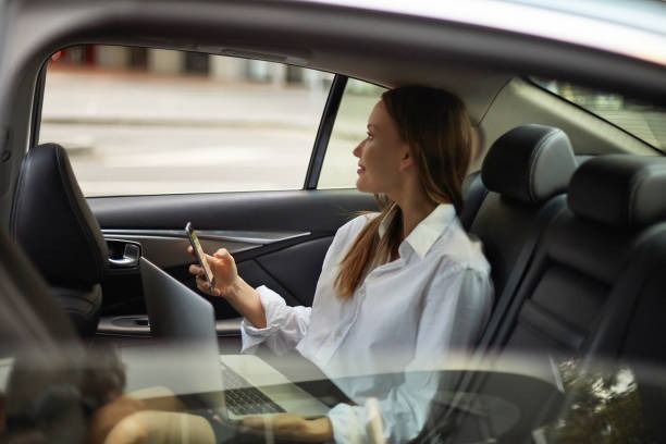 A Woman is Sitting in a Car Using a Laptop and a Cell Phone — Tweed Heads Coolangatta Taxi Service In Banora Point, NSW