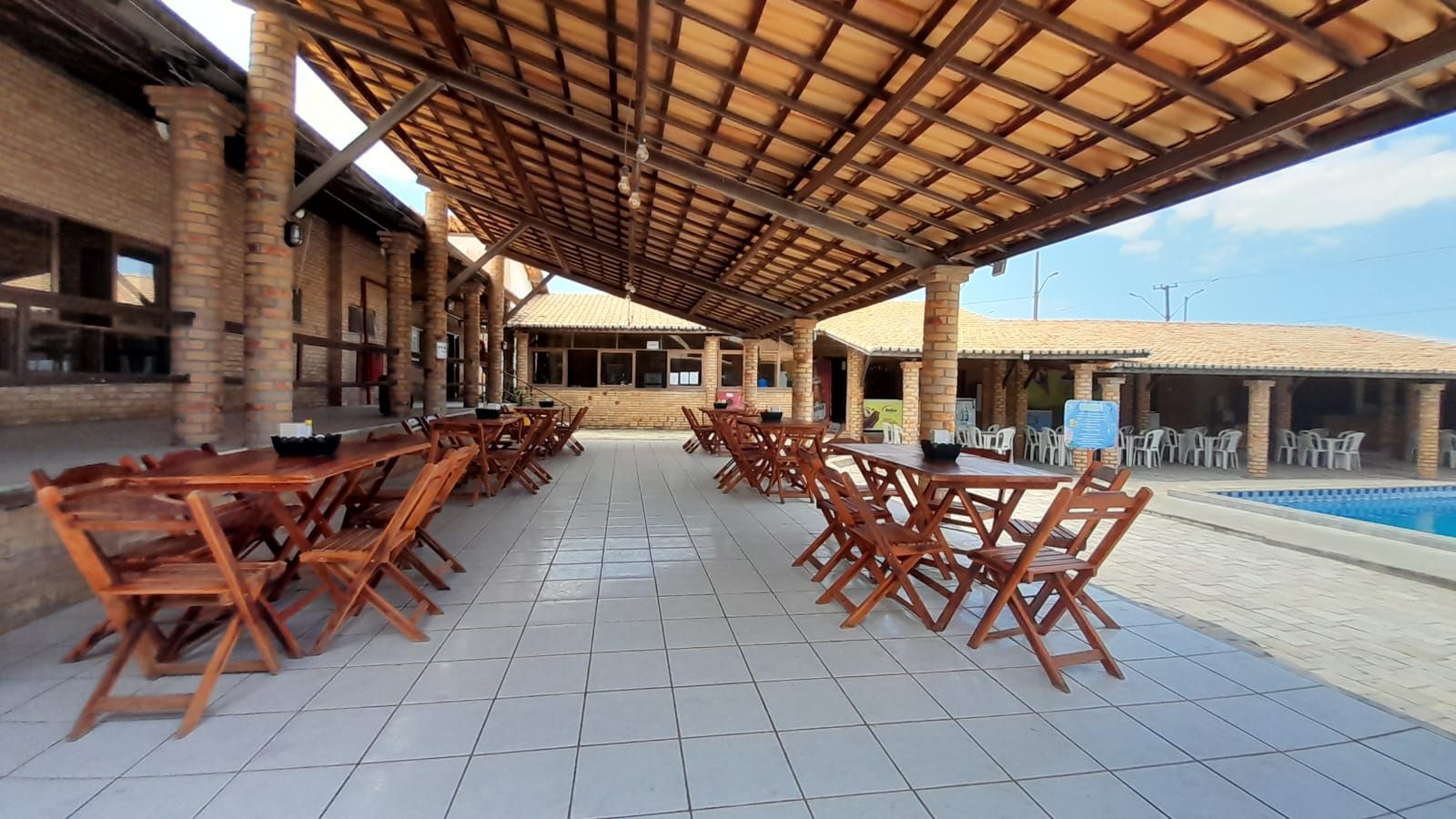 Um restaurante com mesas e cadeiras sob uma cobertura com vista para uma piscina.